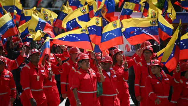 Trabajadores de Pdvsa, vestidos de rojo y ondeando banderas, participan en un desfile militar.