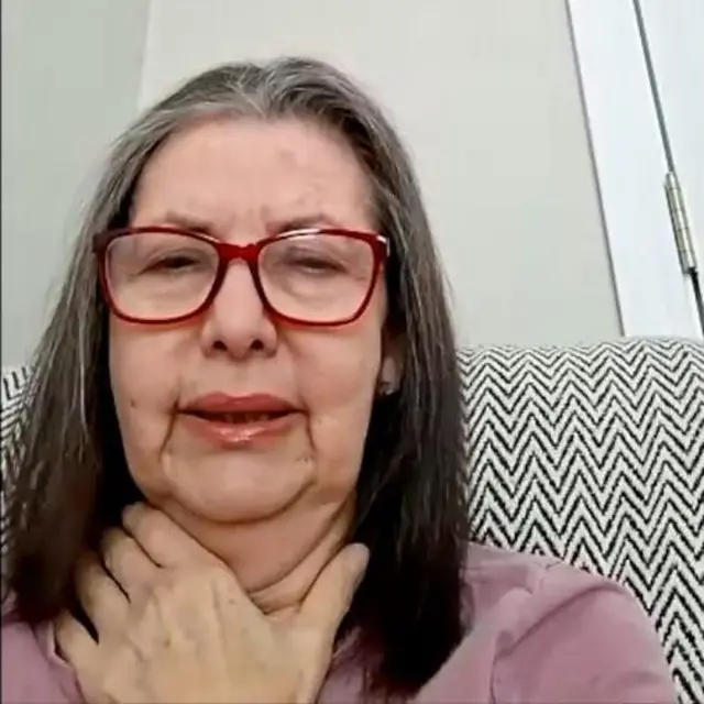 María Elena Uzcátegui usa unos lentes de montura vinotinto y una camisa rosada. Esta sentada en un sofá de rayas negras y blancas.